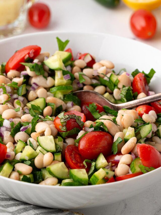 White bean salad with cherry tomatoes, cucumber, red onion, and fresh herbs tossed in a lemon vinaigrette in a white serving bowl.