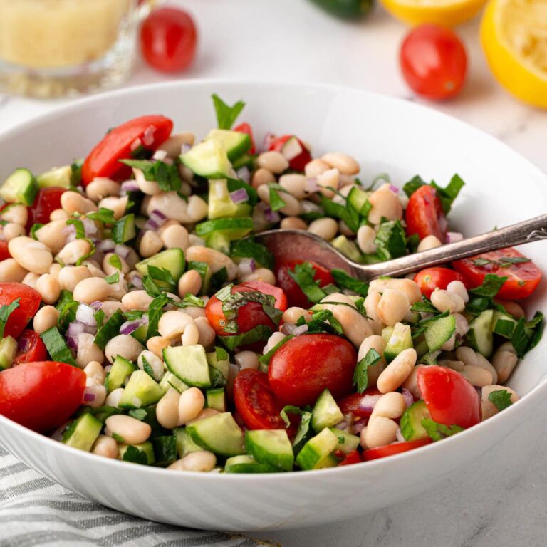 White bean salad with cherry tomatoes, cucumber, red onion, and fresh herbs tossed in a lemon vinaigrette in a white serving bowl.