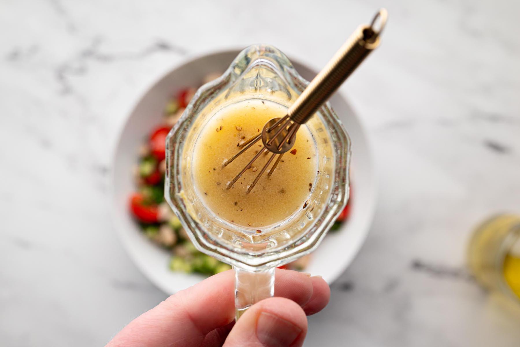 Lemon vinaigrette made with olive oil, lemon juice, Dijon mustard, honey, salt, and black pepper being whisked in a small glass container.