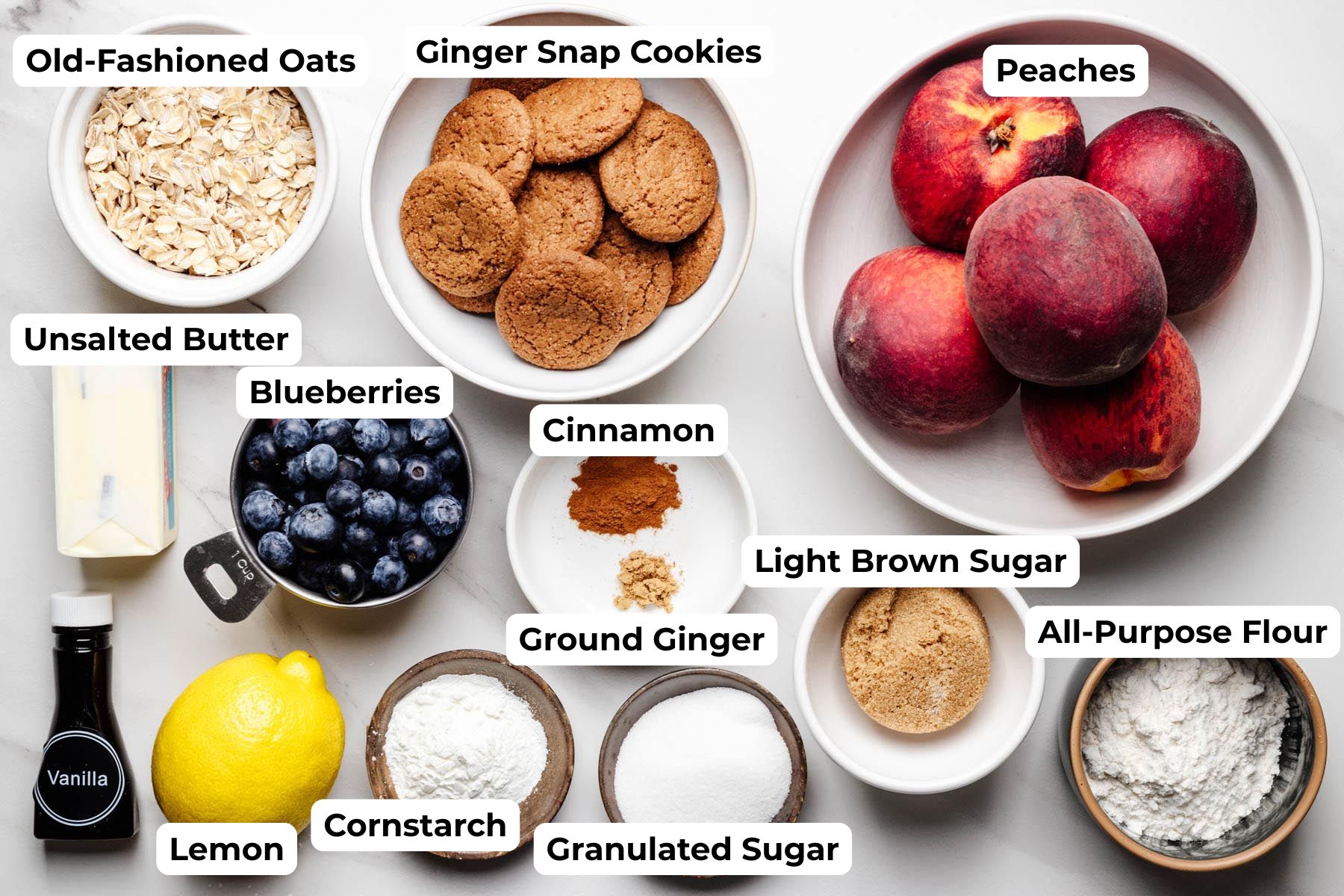 Ingredients for blueberry peach crisp, including peaches, blueberries, ginger snap cookies, oats, butter, flour, sugars, lemon, vanilla, cornstarch, cinnamon, and ginger.