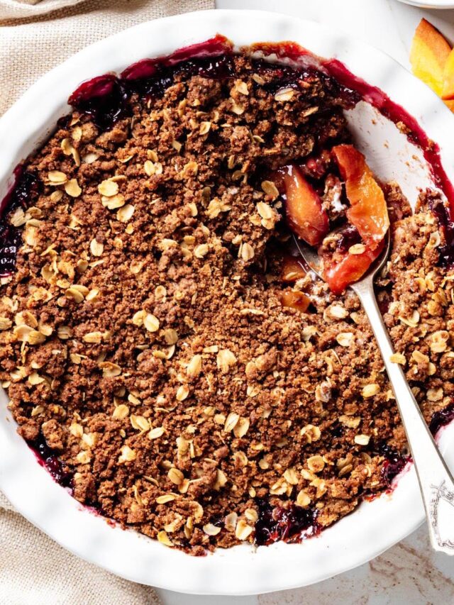 Blueberry peach crisp in a white baking dish with a spoon lifting a serving to reveal the juicy peach and blueberry filling beneath the oat crumble topping.