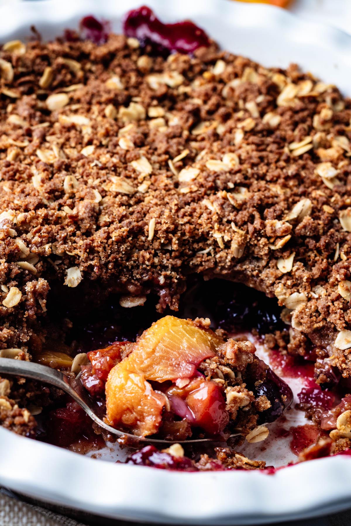 Close-up of a spoonful of blueberry peach crisp showing juicy peaches, blueberries, and crisp oat topping.