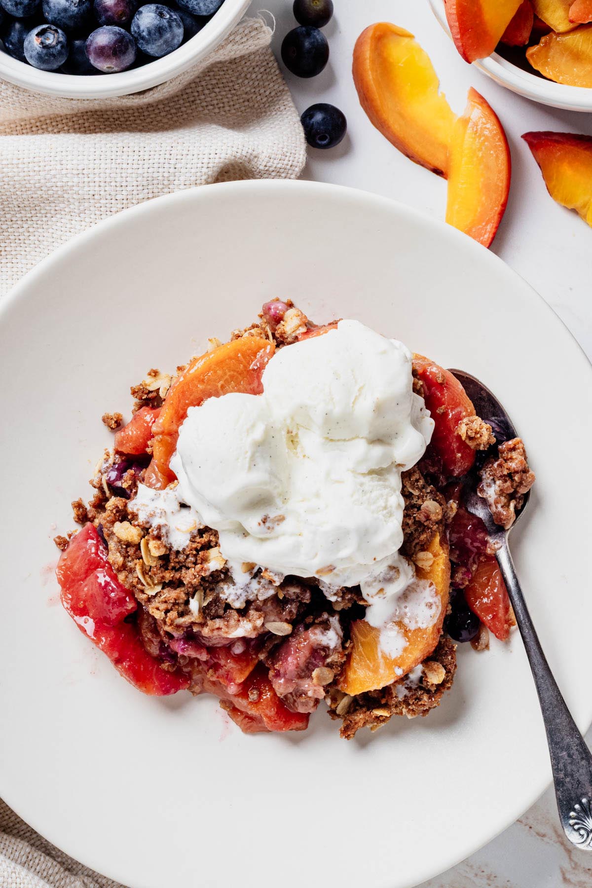 Serving of blueberry peach crisp topped with vanilla ice cream in a shallow bowl.