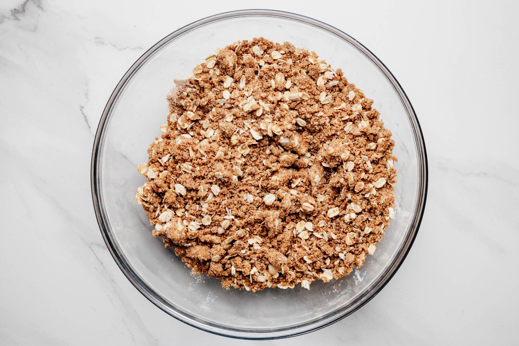 Prepared ginger snap oat topping with visible crumbly clusters in a glass mixing bowl.