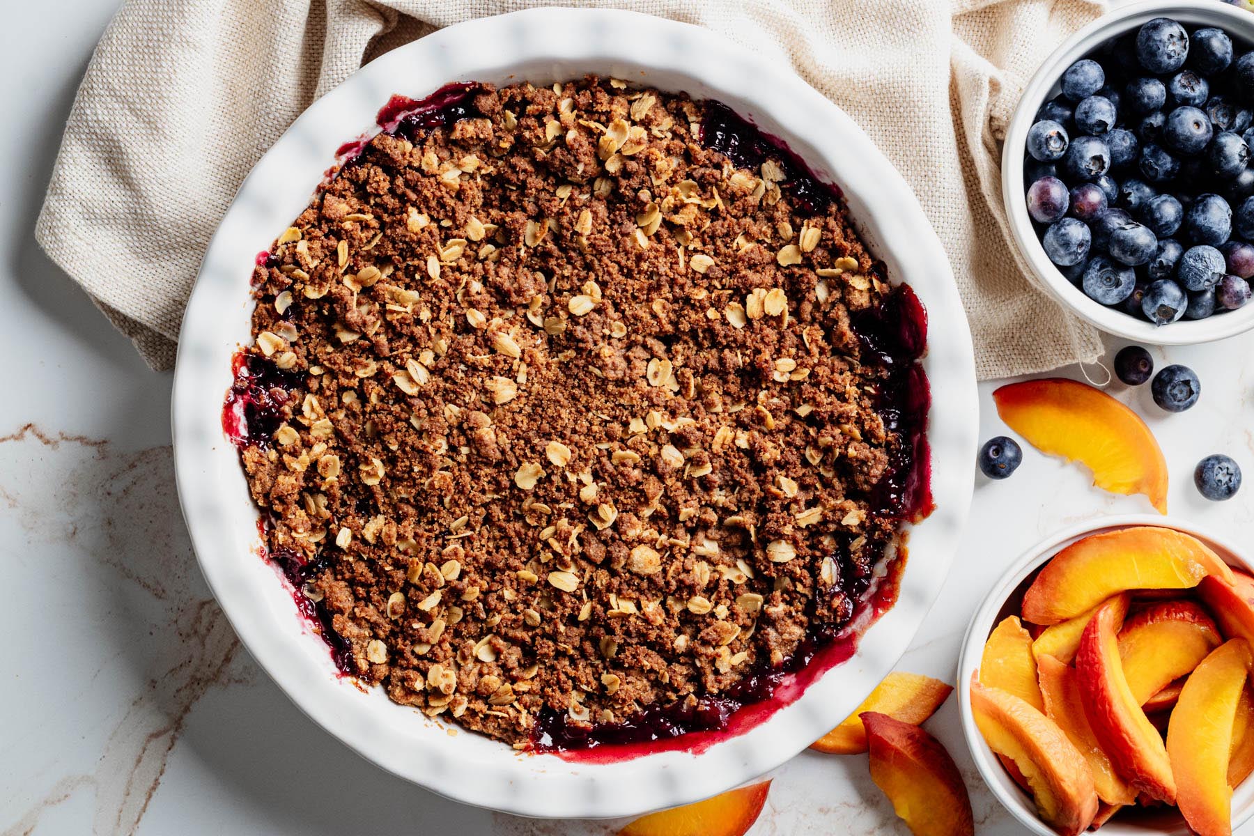 Baked blueberry peach crisp with a golden brown ginger snap oat topping and blueberry filling bubbling around the edges.