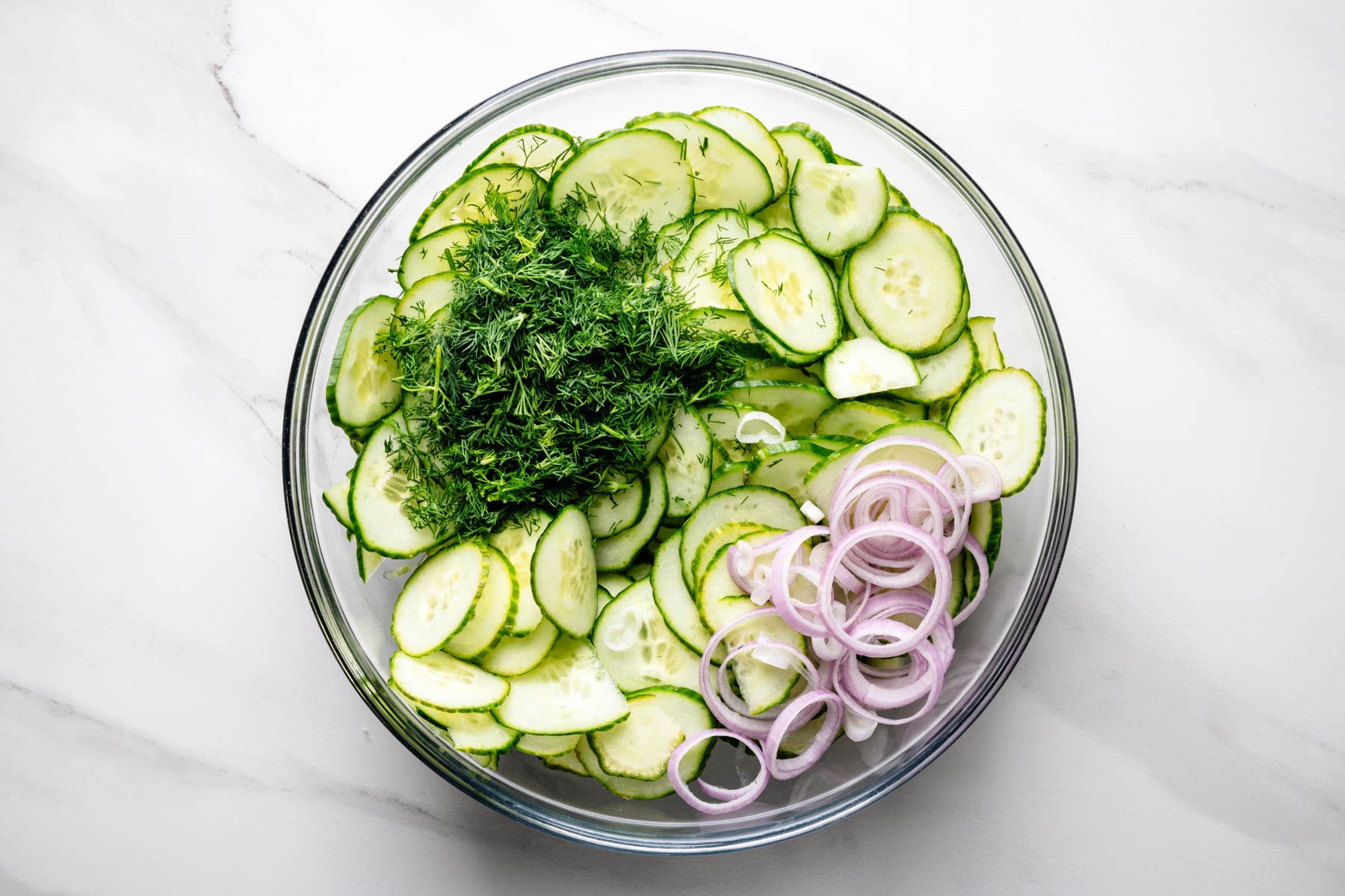 Thinly sliced English cucumbers, fresh dill, and sliced shallot in a large glass mixing bowl before adding the dressing.