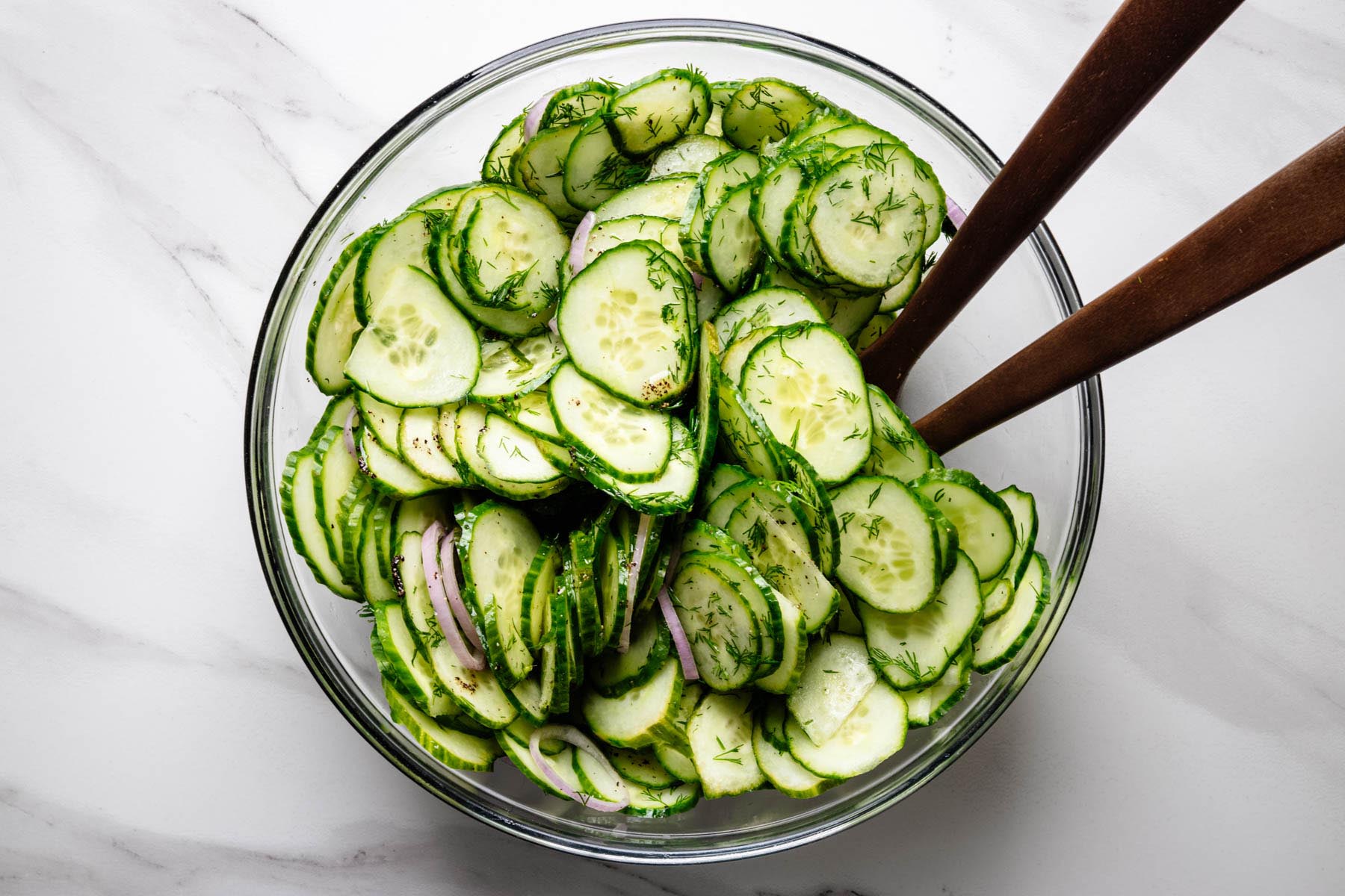 Cucumber dill salad tossed with the white wine vinaigrette in a large glass mixing bowl.