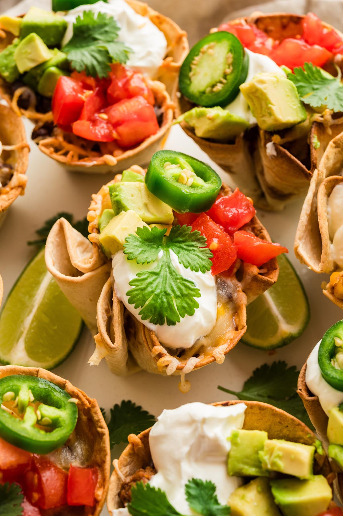 Close-up of enchilada cups filled with seasoned beef and cheese, topped with avocado, tomatoes, jalape&ntilde;os, sour cream, and cilantro.