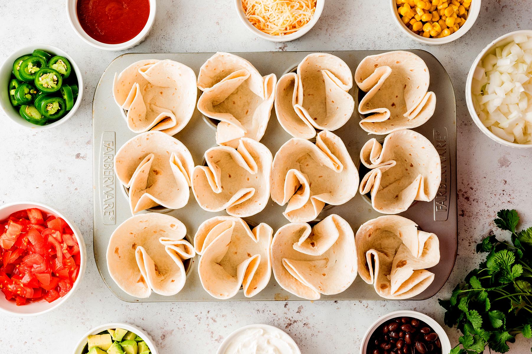 Flour tortillas folded into the cups of a standard muffin tin to create shells for enchilada cups.