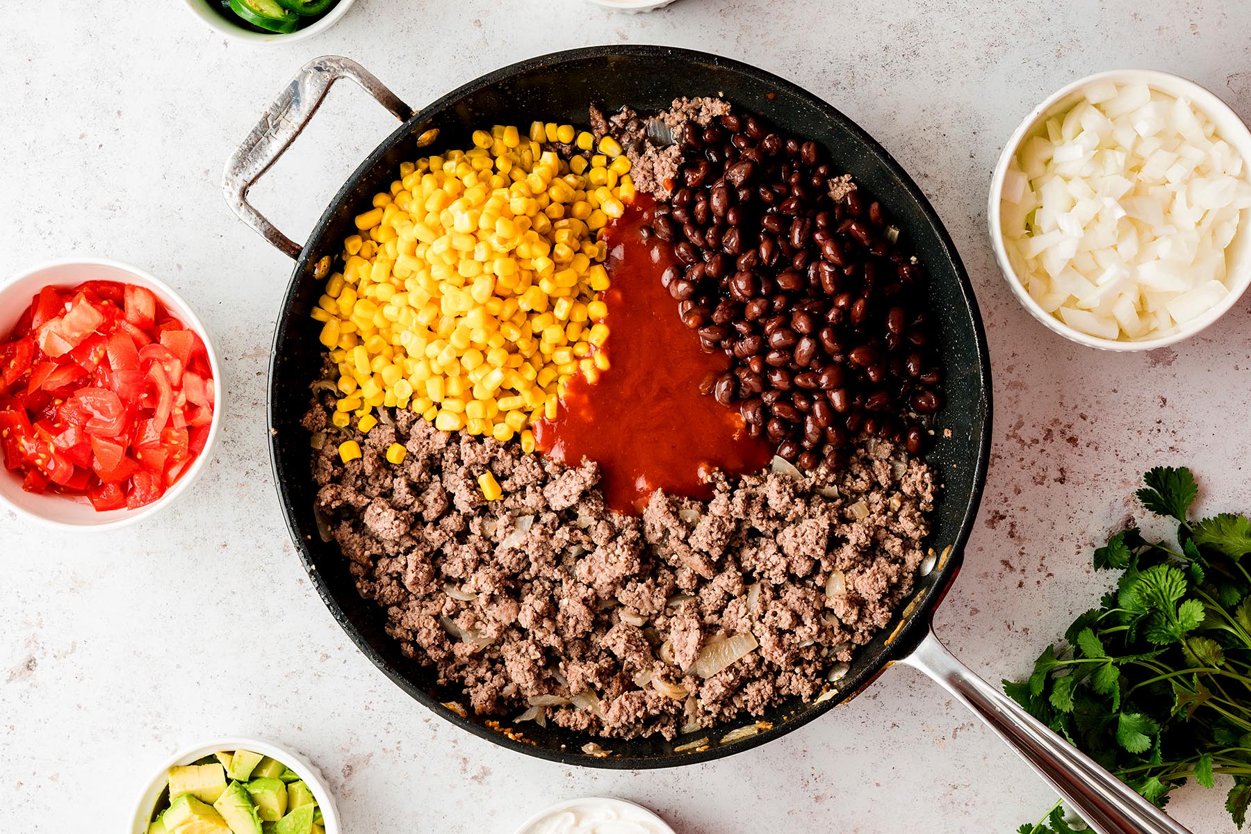 Cooked ground beef in a skillet with black beans, corn, and enchilada sauce added.