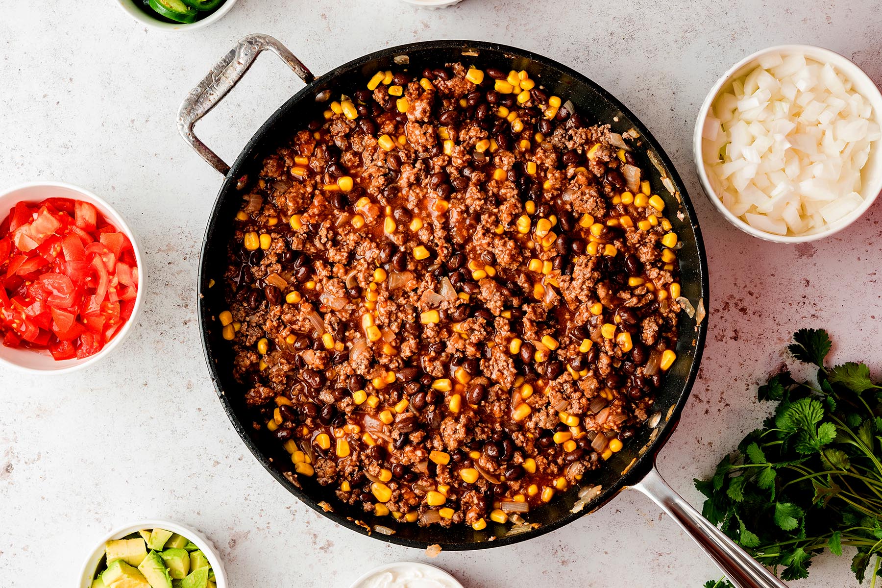 Seasoned beef mixture with black beans, corn, onions, and enchilada sauce cooked together in a skillet.