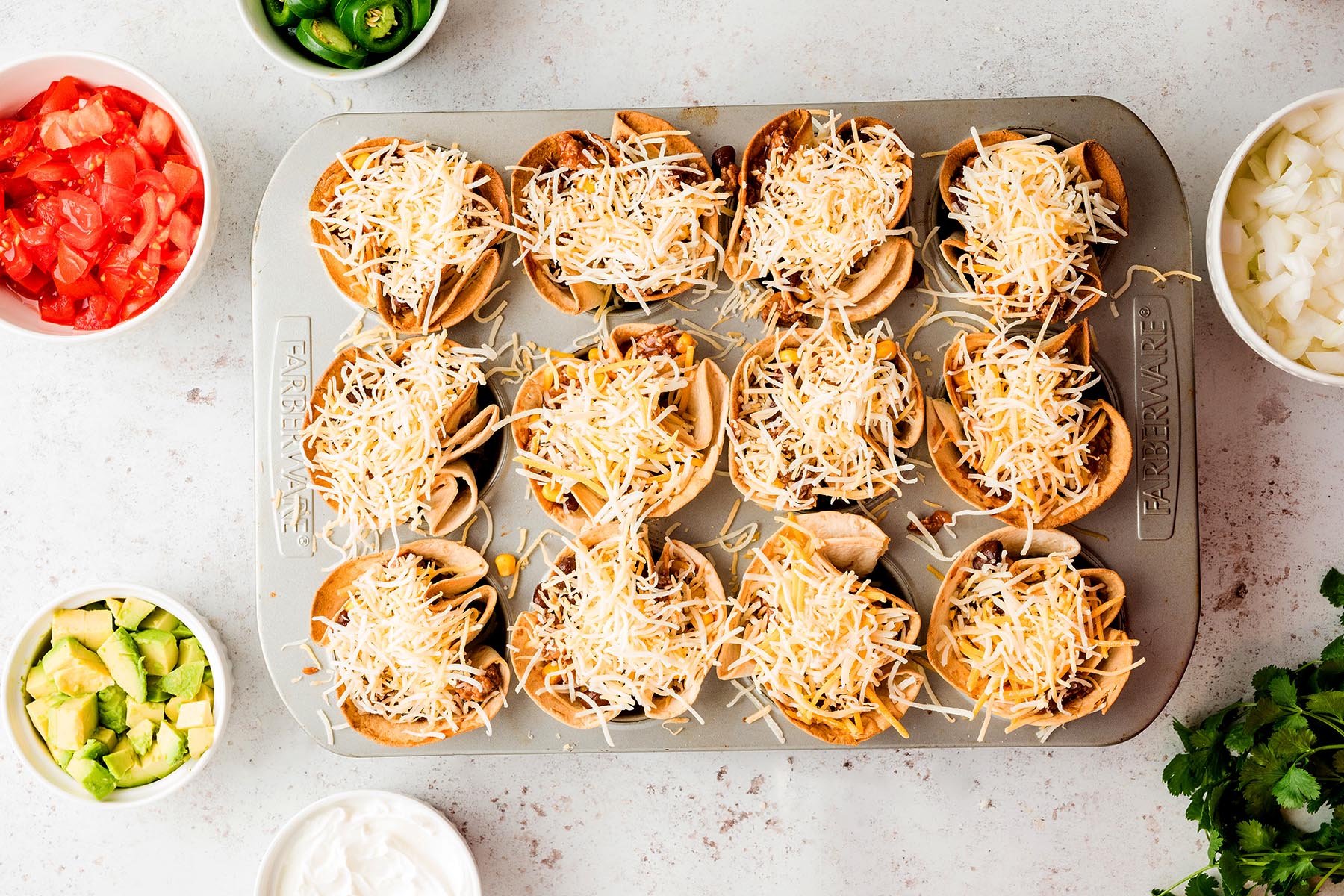 Filled tortilla cups topped with shredded Mexican cheese before baking.