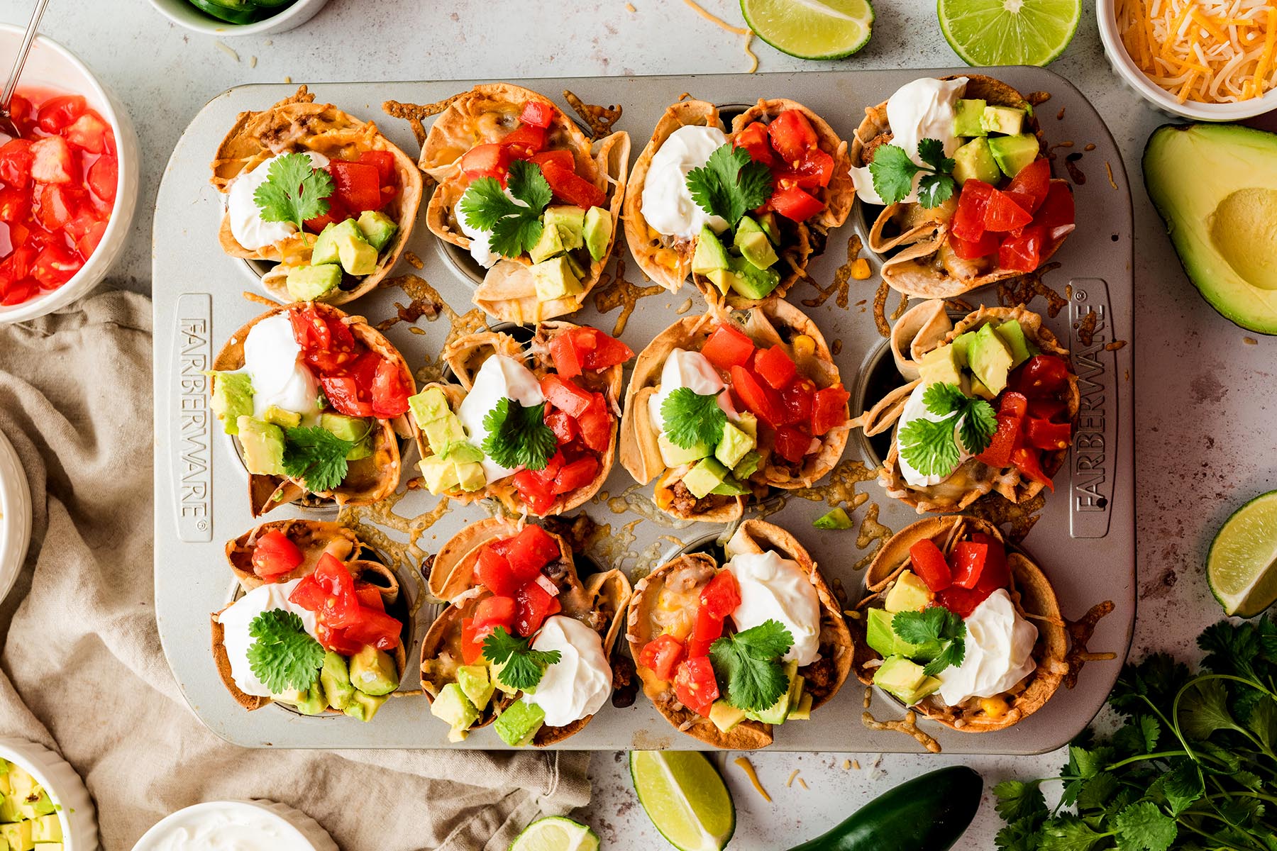 Finished enchilada cups topped with sour cream, diced tomatoes, avocado, jalape&ntilde;os, and cilantro.