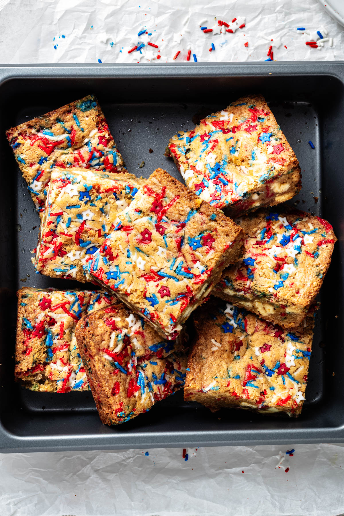 Overhead view of fireworks blondies with white chocolate chunks and red, white, and blue patriotic sprinkles arranged in a baking pan.