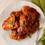 Sticky honey garlic chicken thighs glazed with a glossy sauce and garnished with sesame seeds and sliced green onions on a serving platter.