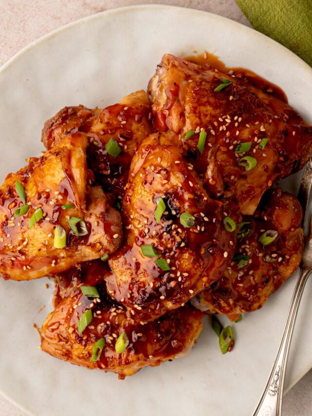 Sticky honey garlic chicken thighs glazed with a glossy sauce and garnished with sesame seeds and sliced green onions on a serving platter.