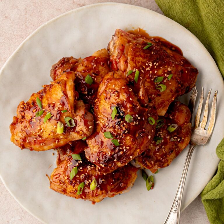 Sticky honey garlic chicken thighs glazed with a glossy sauce and garnished with sesame seeds and sliced green onions on a serving platter.
