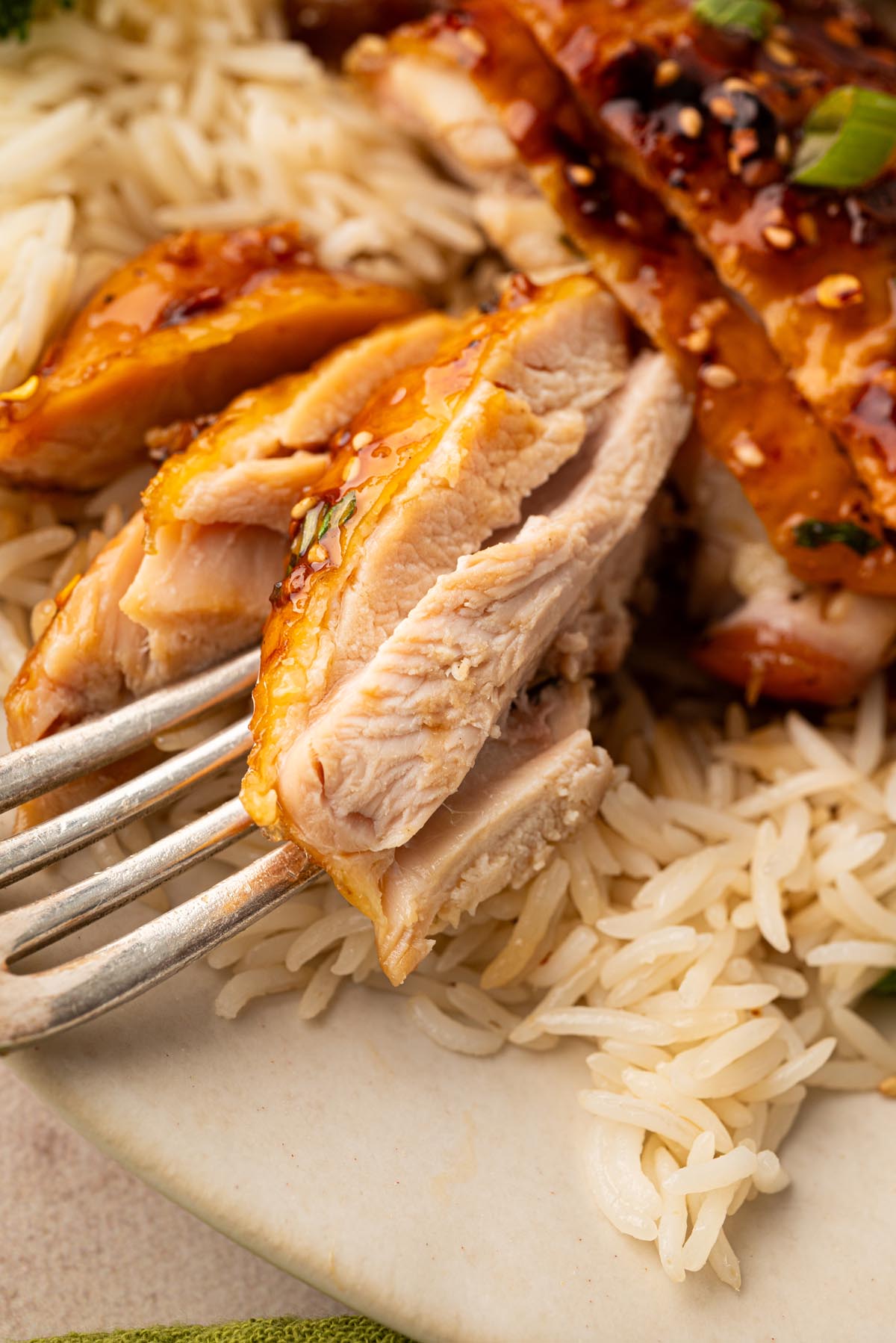 Close-up of a juicy honey garlic chicken thigh on a fork, showing the tender interior with white rice in the background.