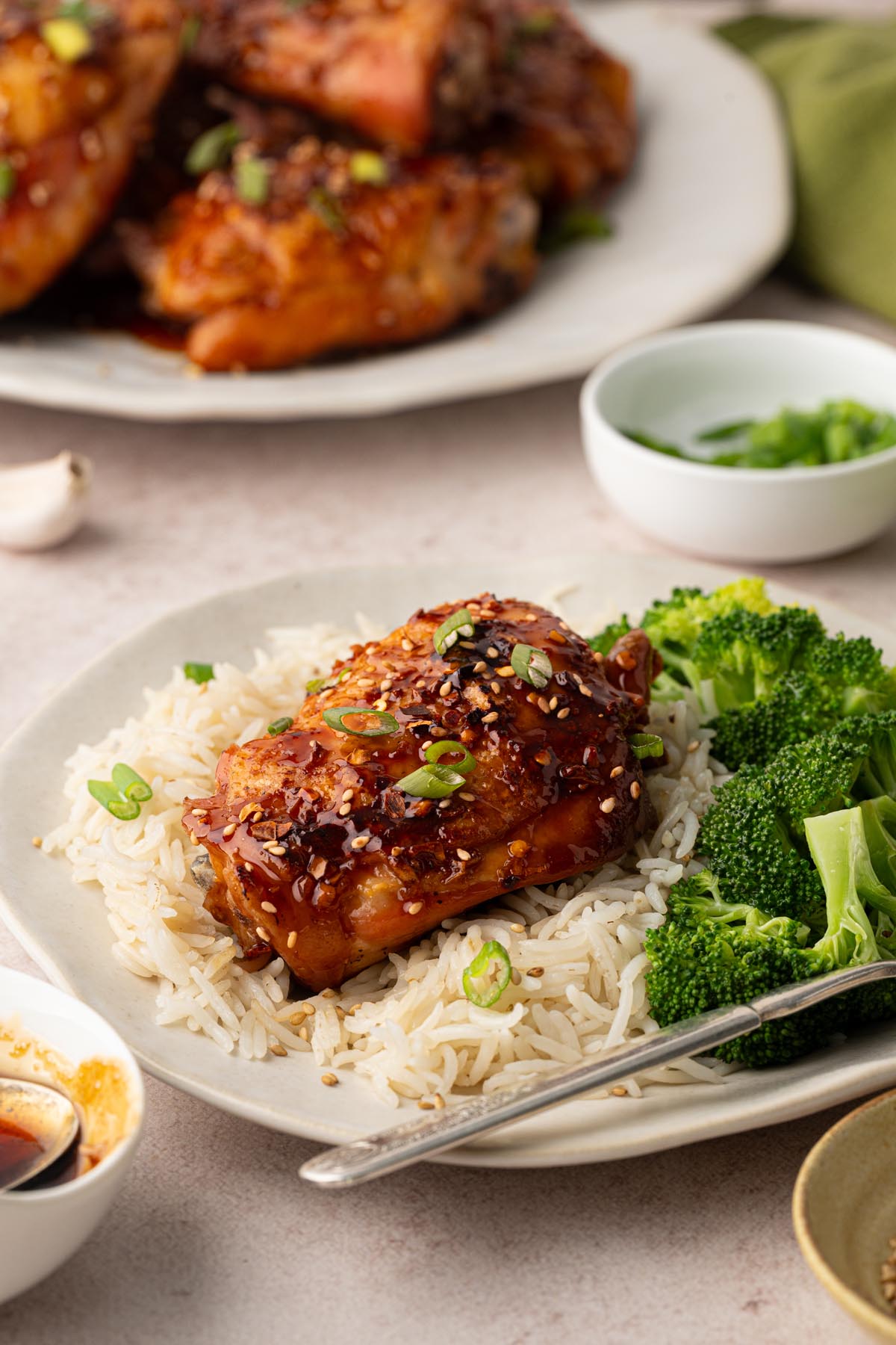 Honey garlic chicken thigh served over white rice with steamed broccoli, garnished with sesame seeds and sliced green onions.