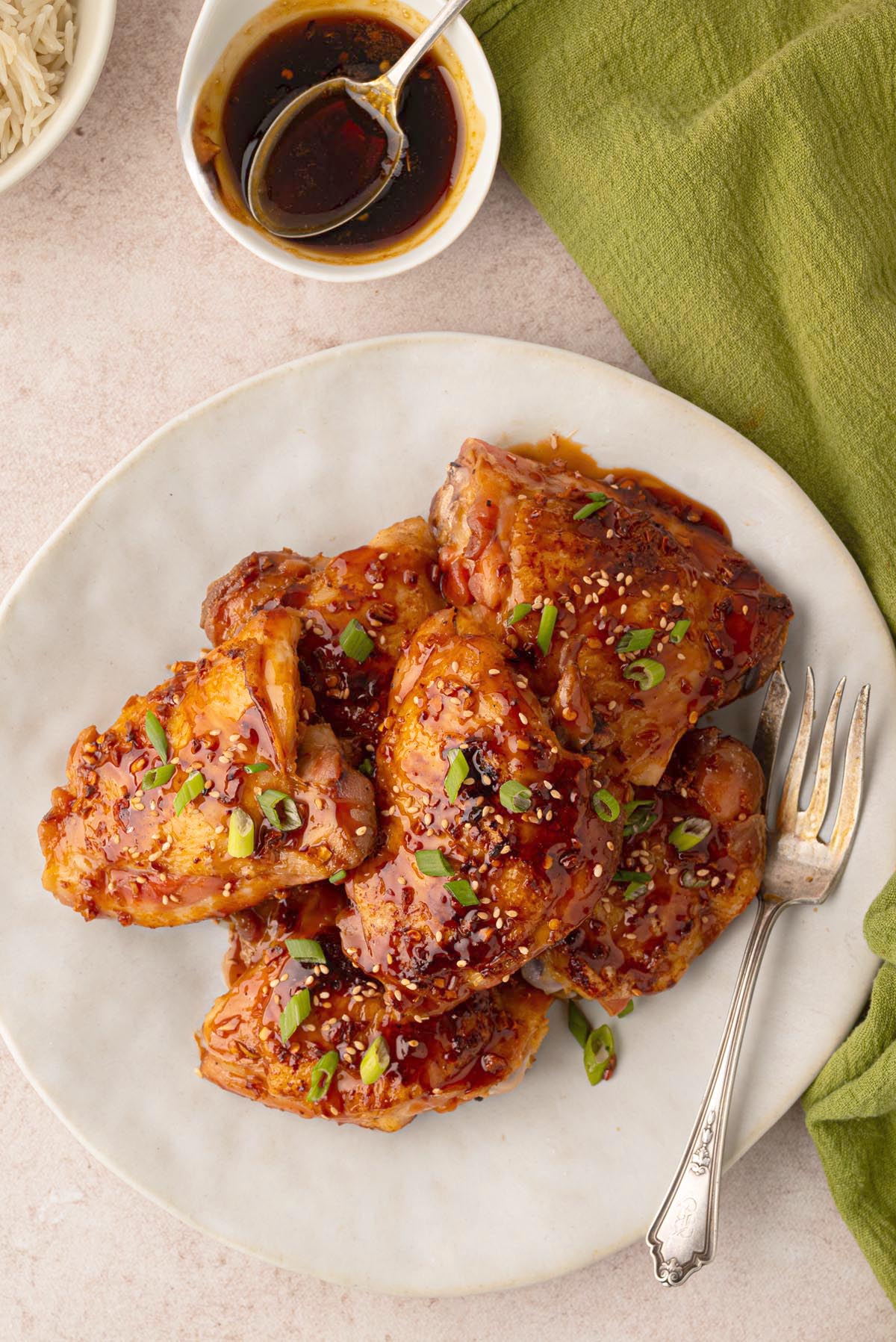 Honey garlic chicken thighs glazed with a sticky sauce and garnished with sesame seeds and sliced green onions on a serving platter.