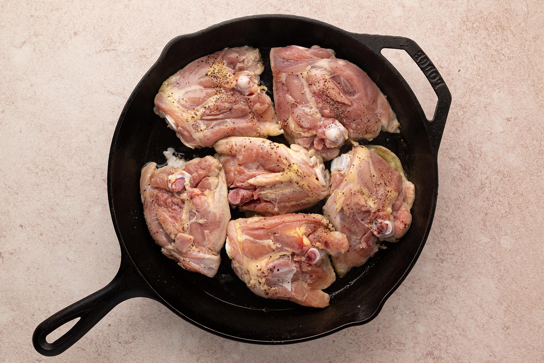 An overhead view of bone-in, skin-on chicken thighs browning skin-side down in a cast iron skillet.