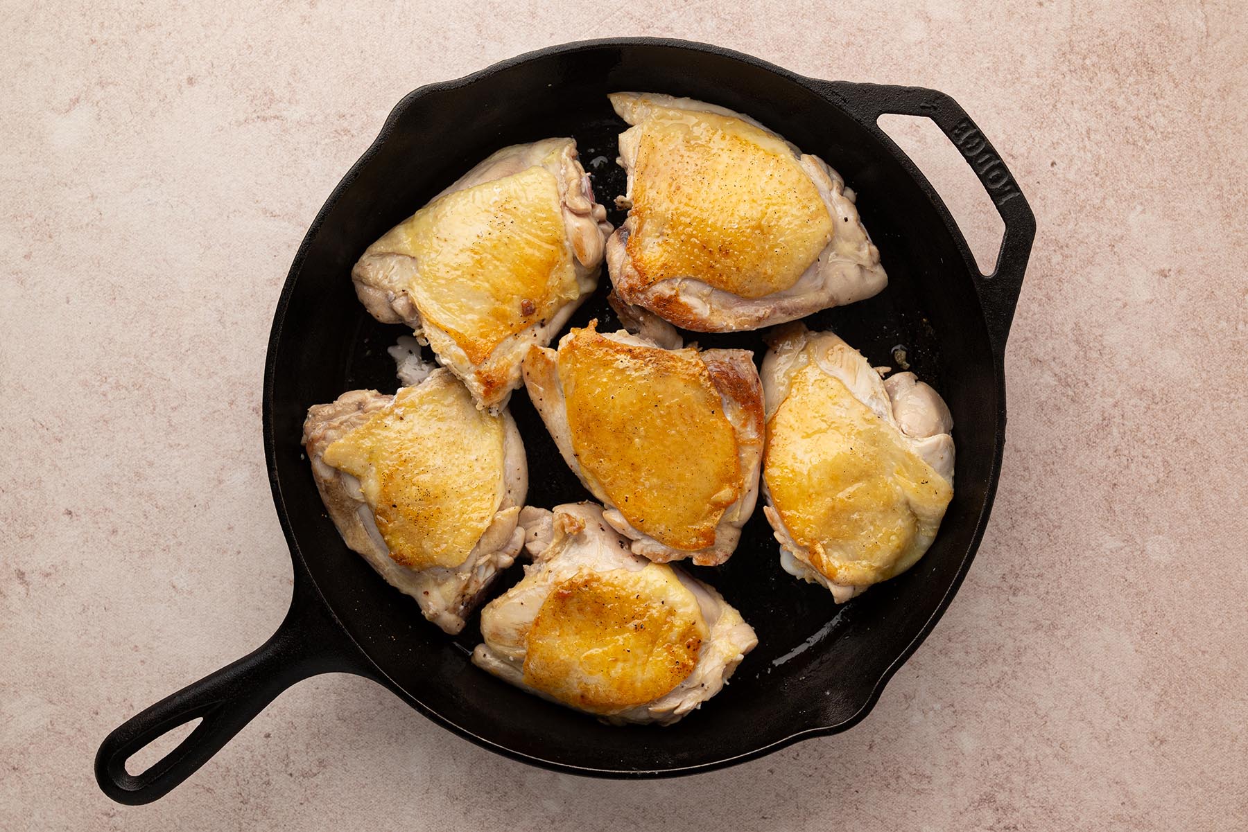 An overhead view of browned chicken thighs turned over in a cast iron skillet. This image shows the chicken after being flipped.