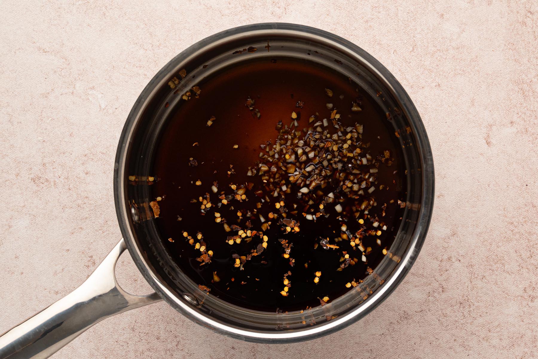 An overhead view of honey, soy sauce, garlic, and red pepper flakes combined in a saucepan.