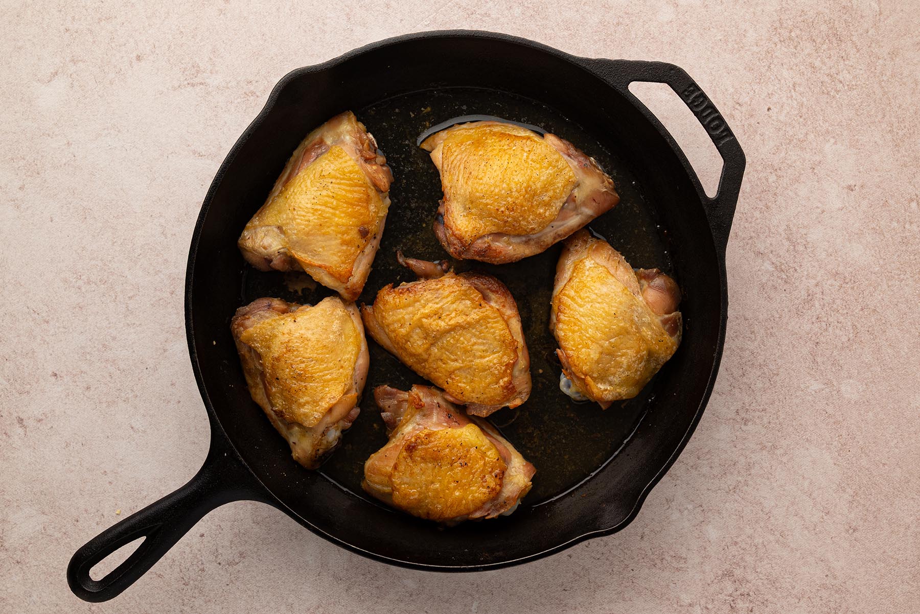 An overhead view of browned chicken thighs returned to a cast iron skillet.