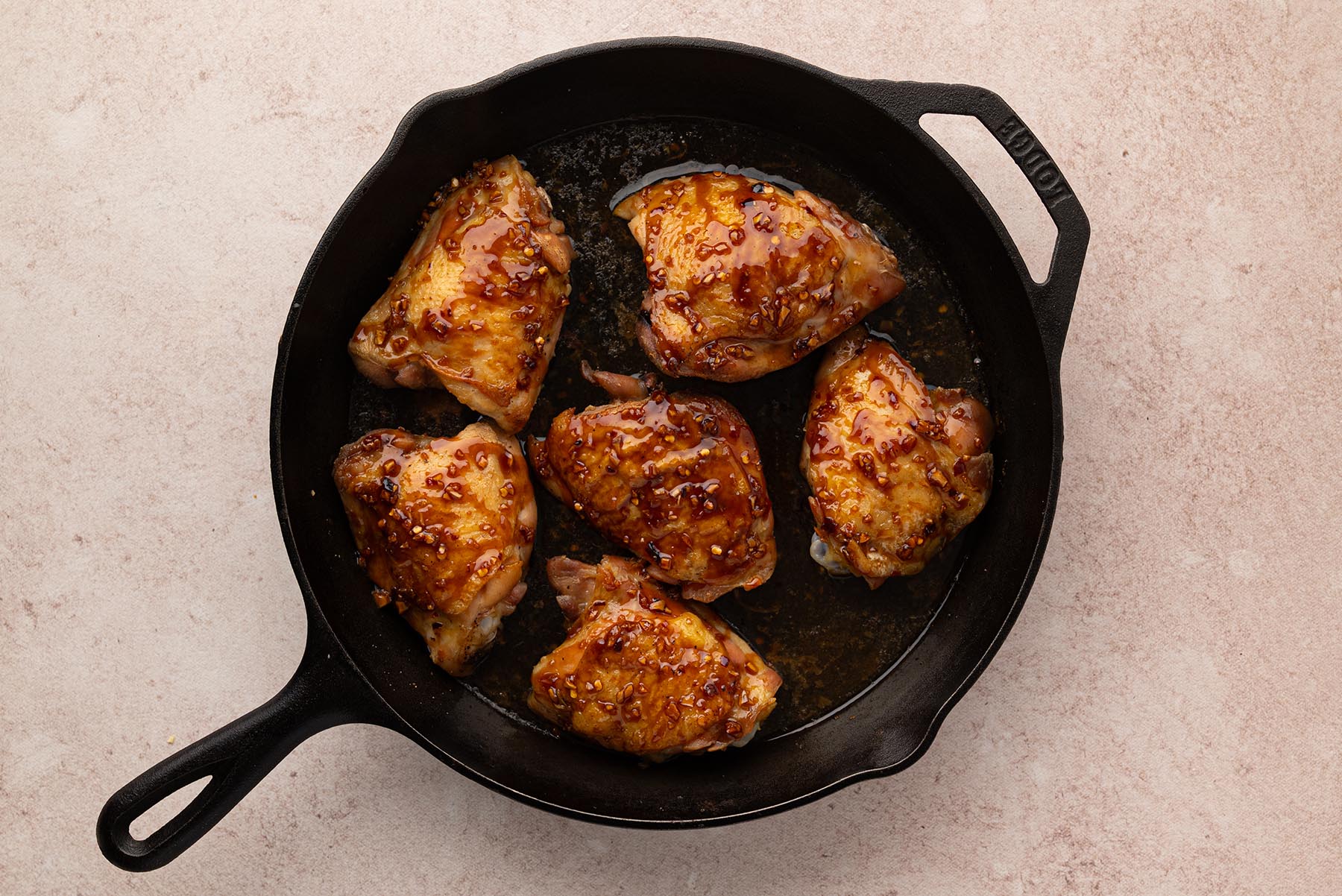 An overhead view of chicken thighs coated with honey garlic sauce in a cast iron skillet.