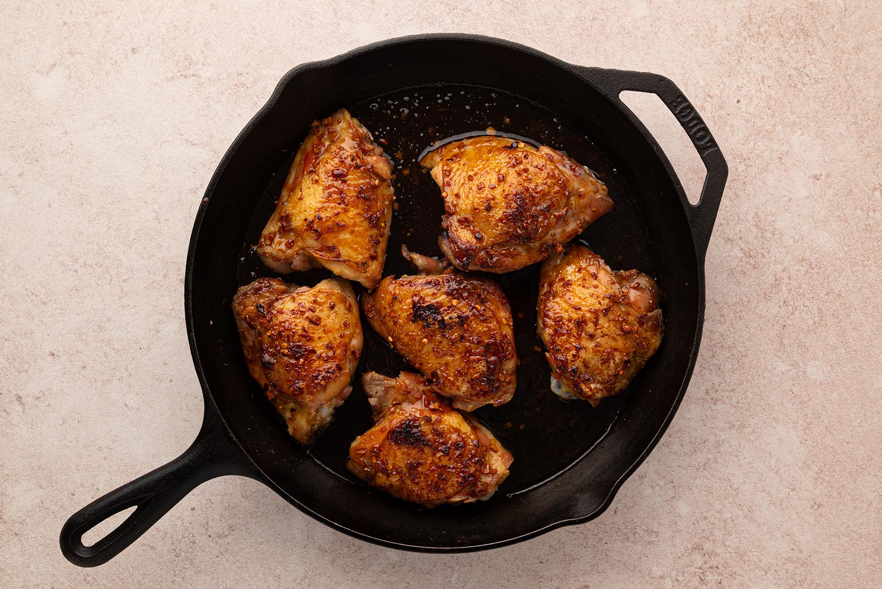 An overhead view of caramelized honey garlic chicken thighs in a cast iron skillet after broiling.