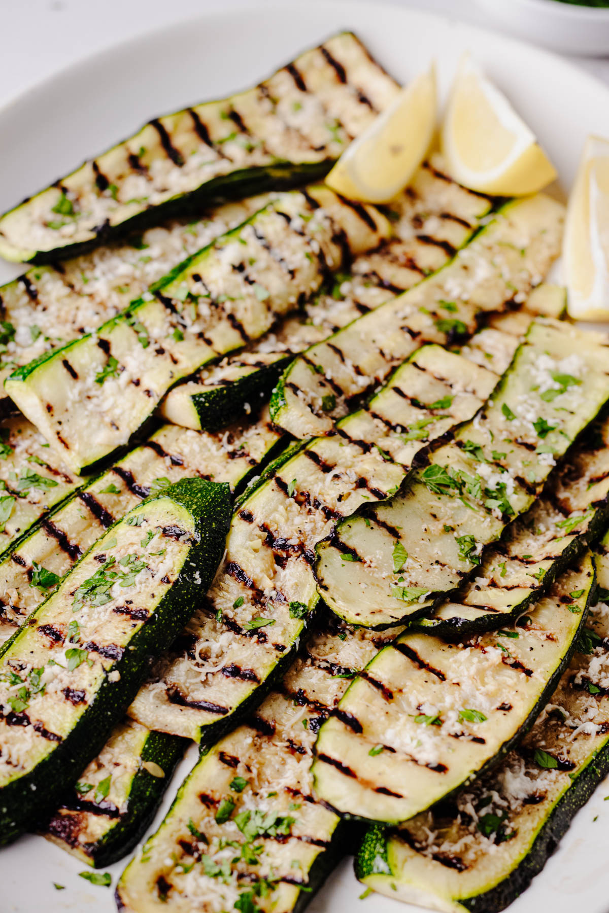 Close-up of grilled zucchini slices topped with grated Parmesan cheese and chopped fresh parsley, showing the charred grill marks and tender texture.