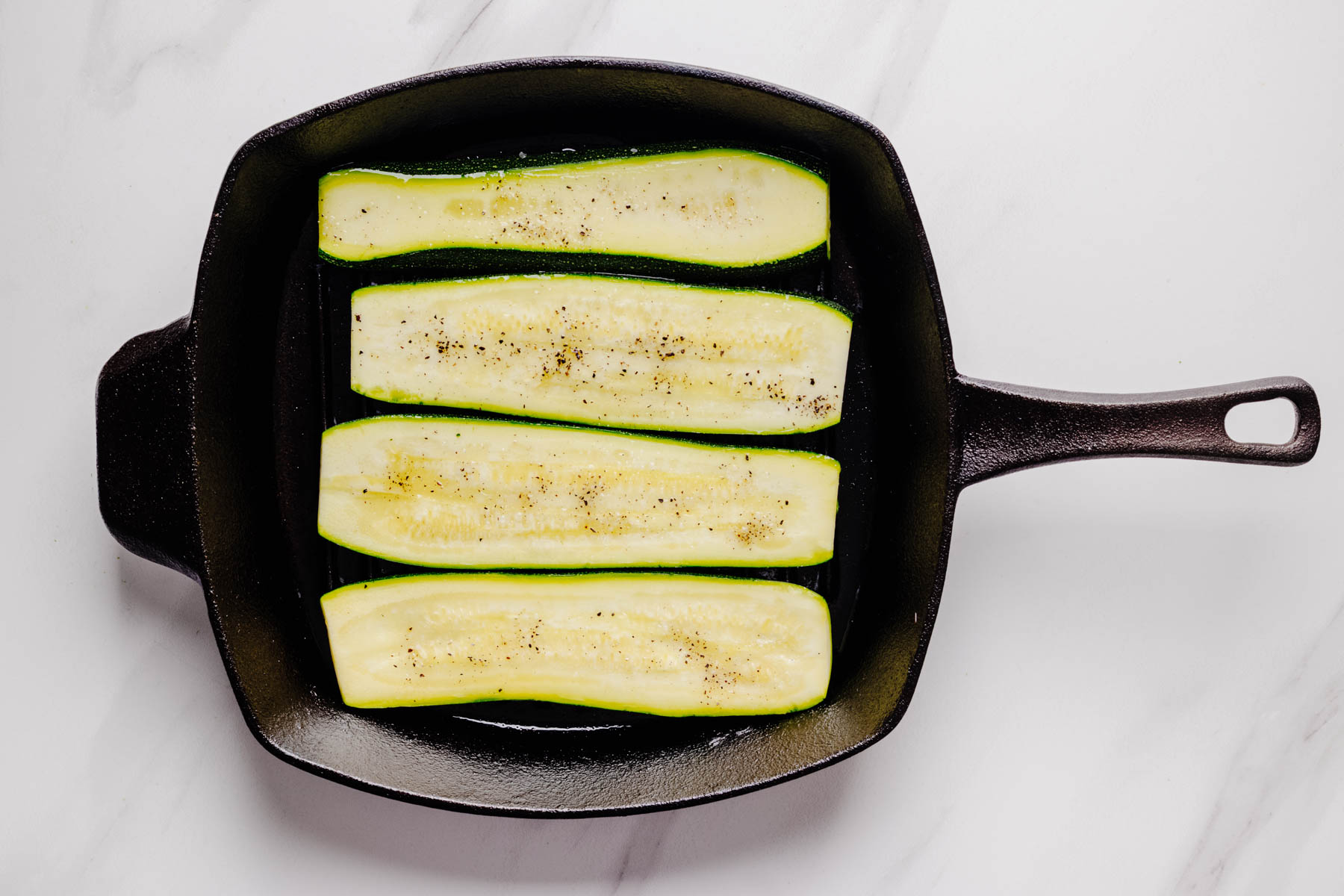 Four zucchini planks cooking on a cast iron grill pan.
