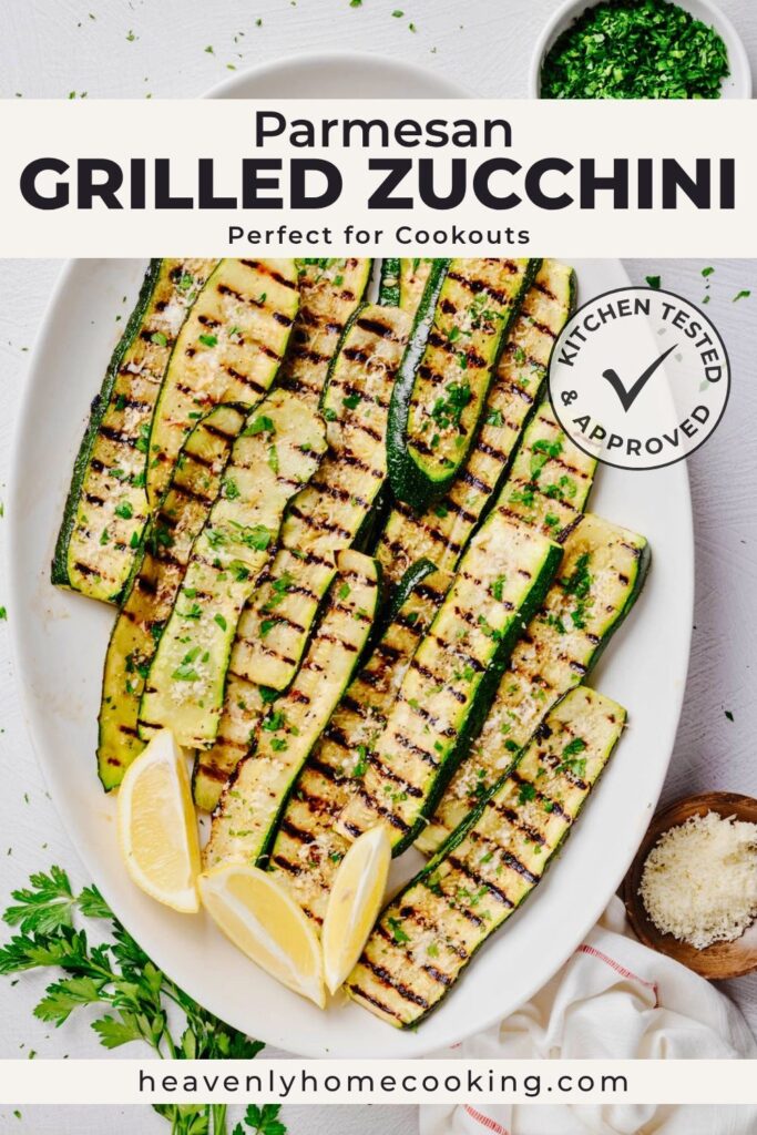 Grilled zucchini topped with grated Parmesan, fresh parsley, and lemon wedges on a white serving platter. Vertical Pinterest pin for a homemade Parmesan Grilled Zucchini recipe from Heavenly Home Cooking.