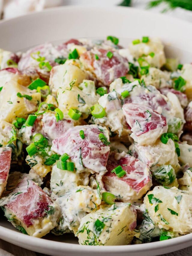 Close-up of creamy red potato salad made with red potatoes, hard-boiled eggs, fresh dill, celery, and green onions in a white serving bowl.