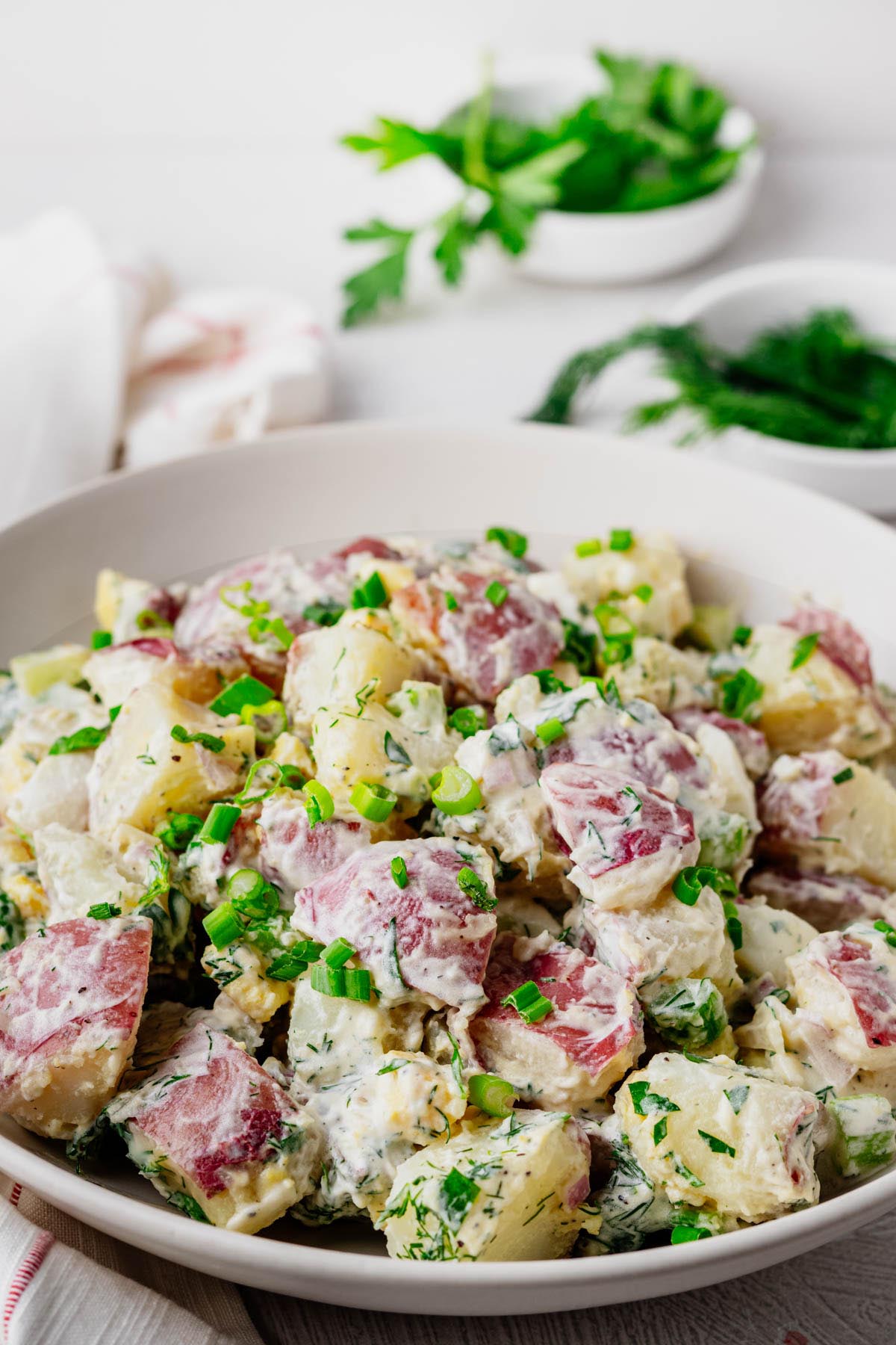 Creamy red potato salad made with red potatoes, hard-boiled eggs, fresh dill, celery, and green onions in a white serving bowl.