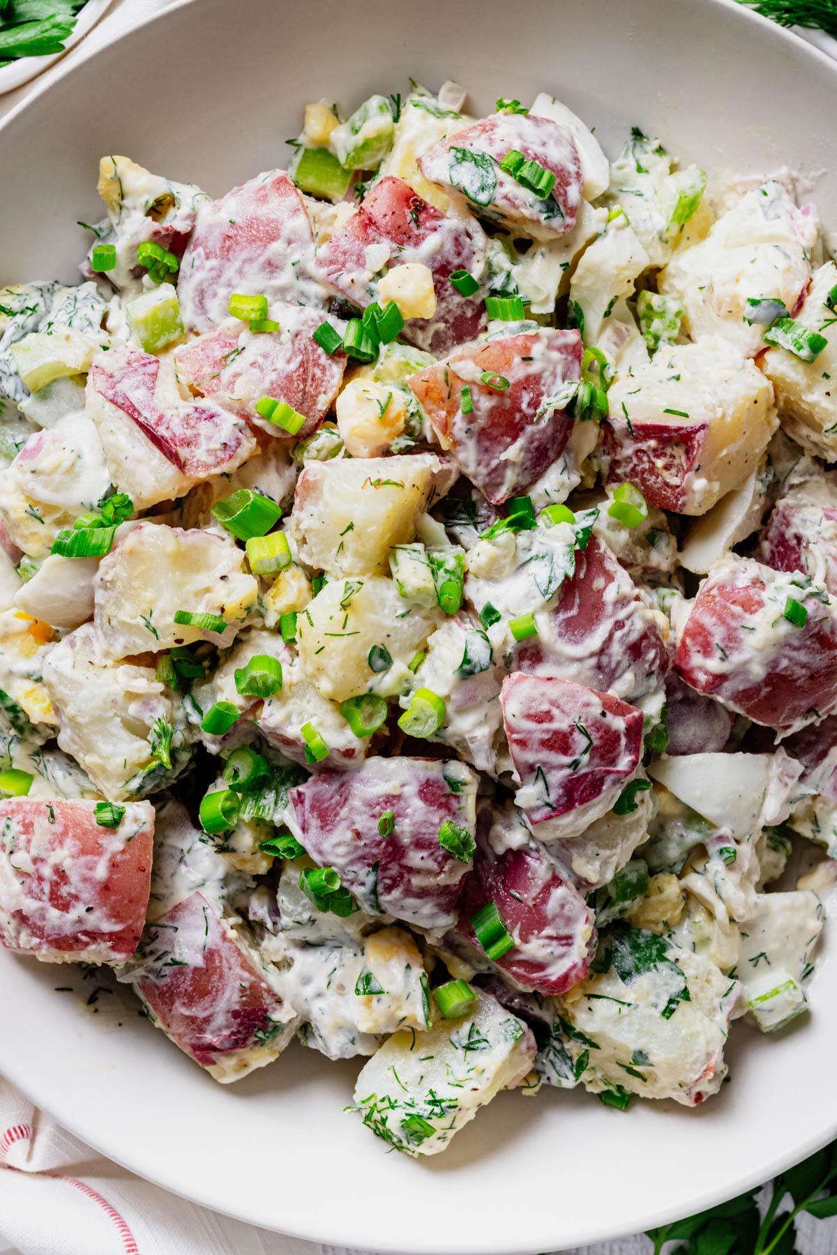 Close-up of creamy red potato salad with red potatoes, hard-boiled eggs, dill, celery, and green onions coated in a tangy dressing.