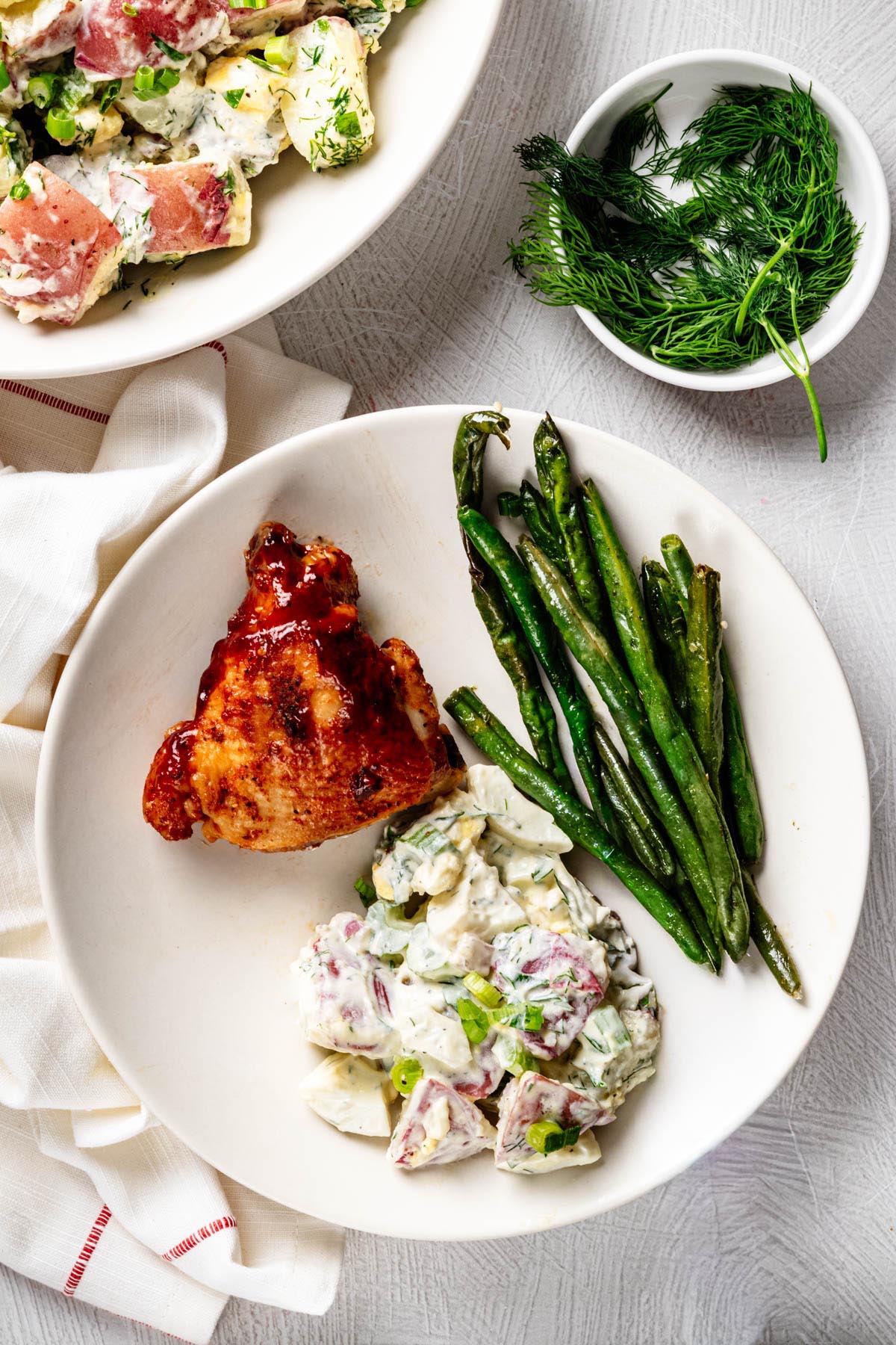 Creamy red potato salad served alongside barbecue chicken and green beans on a white dinner plate.