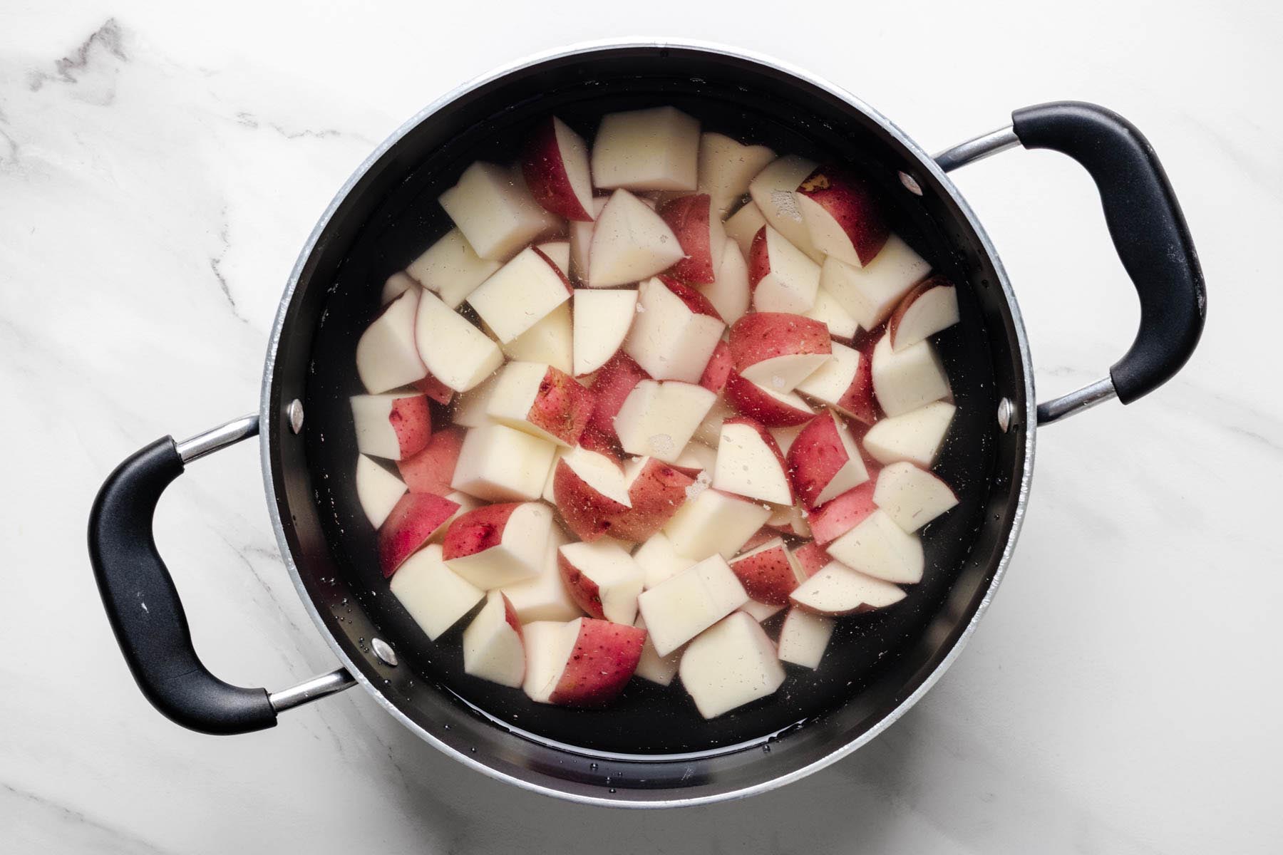 Red potatoes cut into chunks and covered with water in a large pot before cooking.