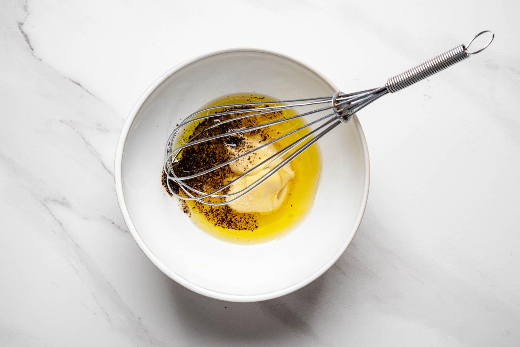 Dijon mustard, apple cider vinegar, olive oil, salt, and black pepper in a bowl with a whisk.