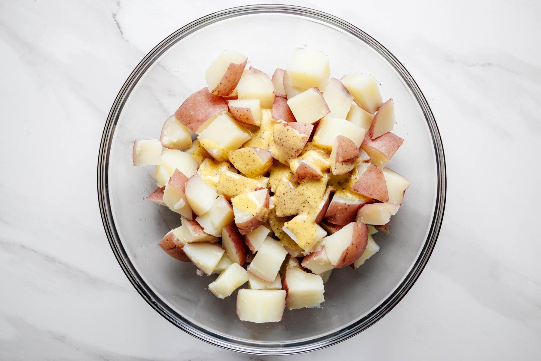 Warm red potatoes in a bowl with Dijon vinaigrette poured over the top.
