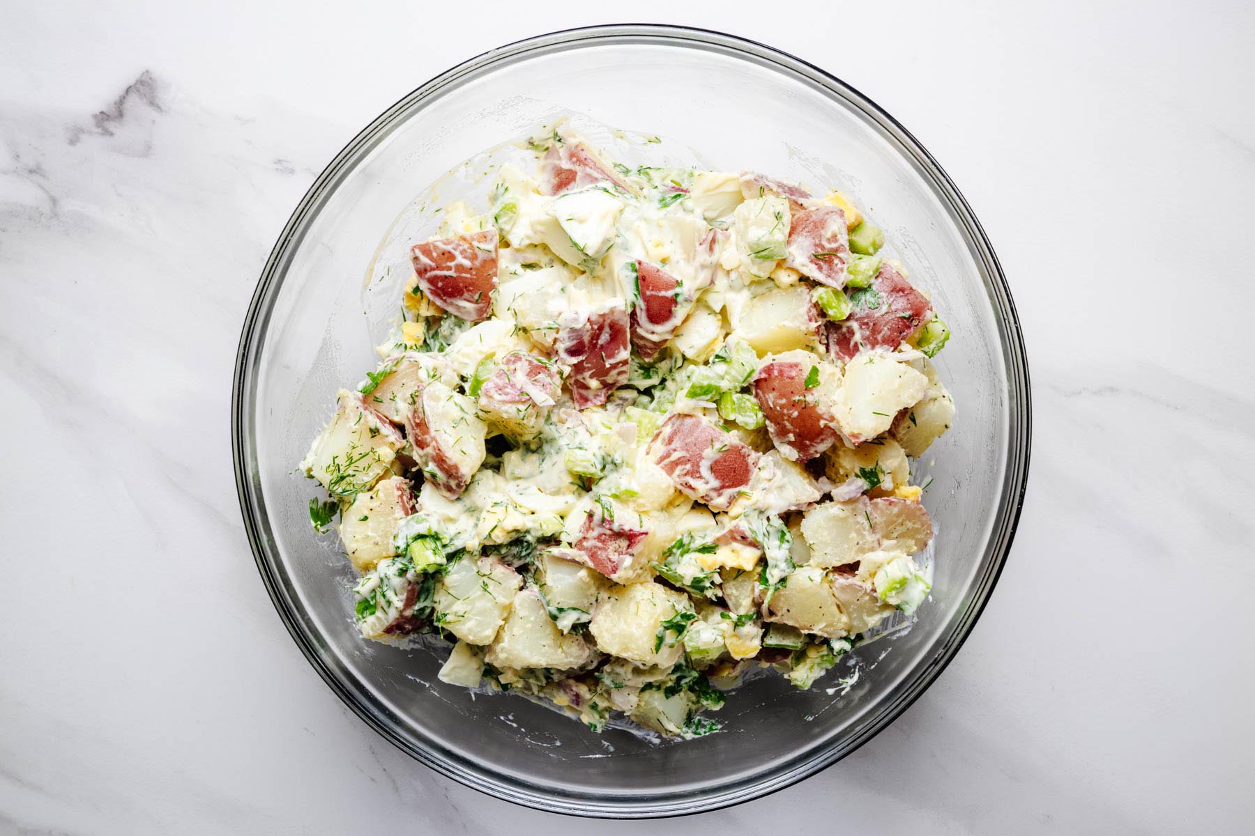 Creamy red potato salad mixed with eggs, celery, dill, parsley, and dressing.