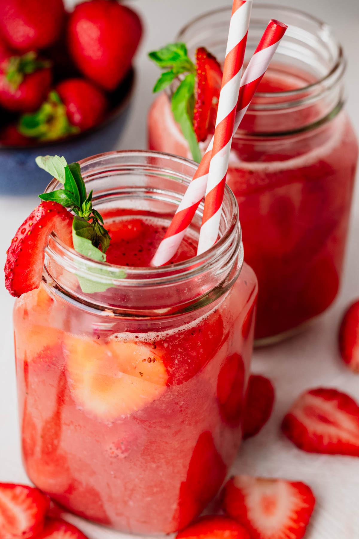 Strawberry agua fresca served in mason jar mugs with fresh strawberry slices, basil garnish, and striped paper straws.