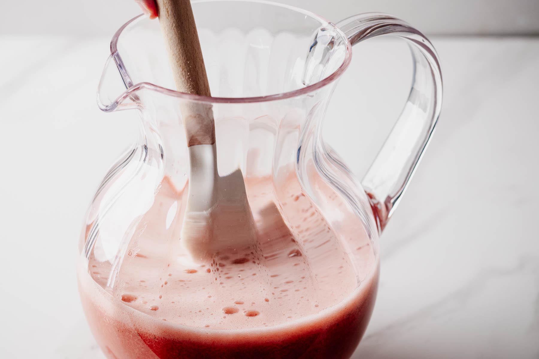 Strawberry basil agua fresca being stirred in a glass pitcher after adding water.
