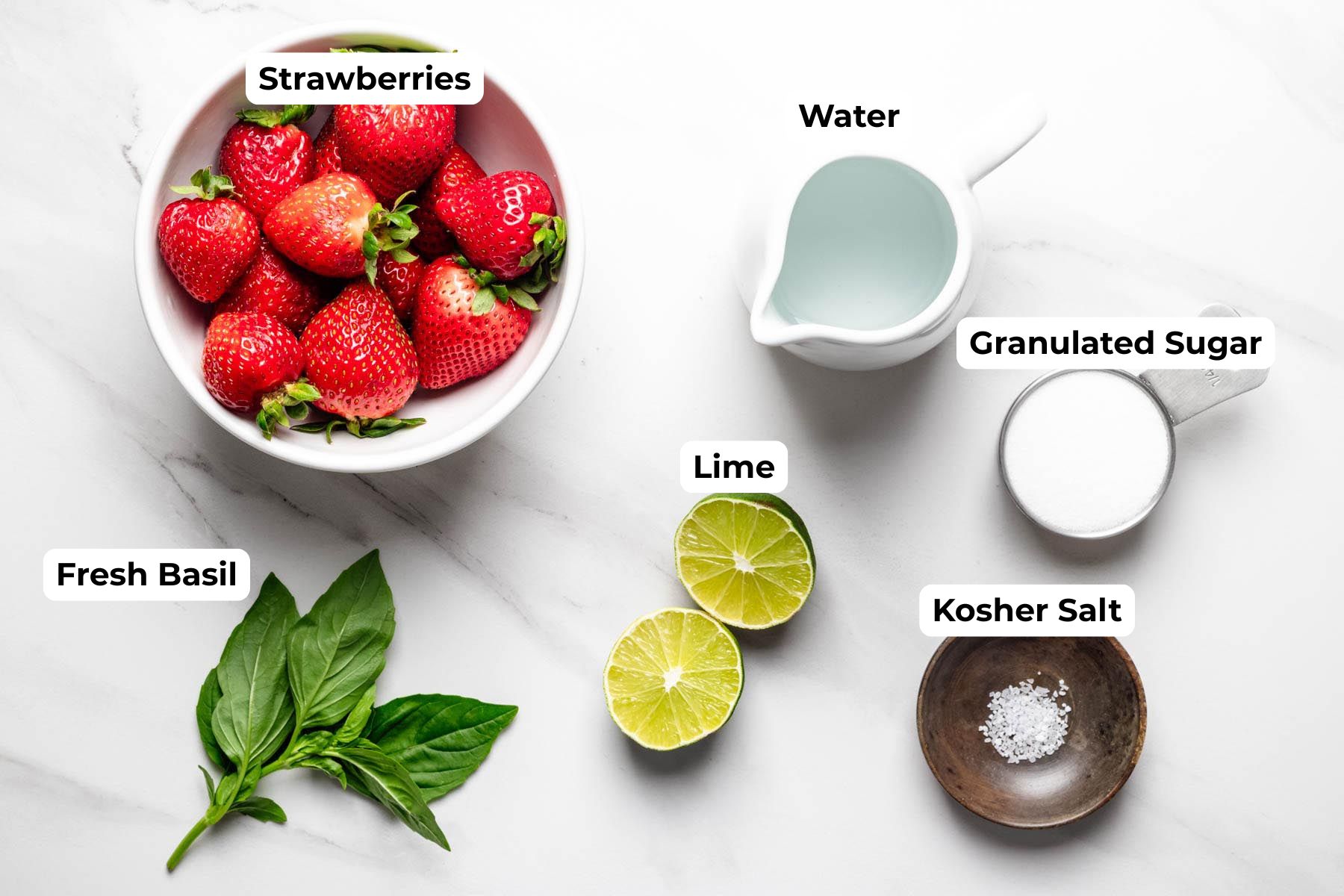 Ingredients for strawberry basil agua fresca including fresh strawberries, basil leaves, lime, sugar, water, and kosher salt arranged on a white surface.