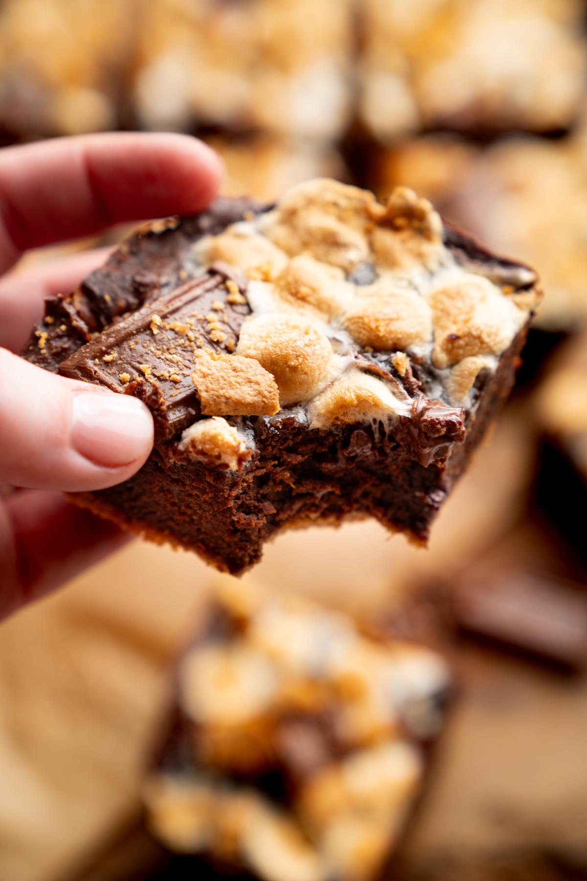 Sweet potato s'mores brownie held in hand, topped with toasted mini marshmallows, melted chocolate, and graham cracker crumbs.
