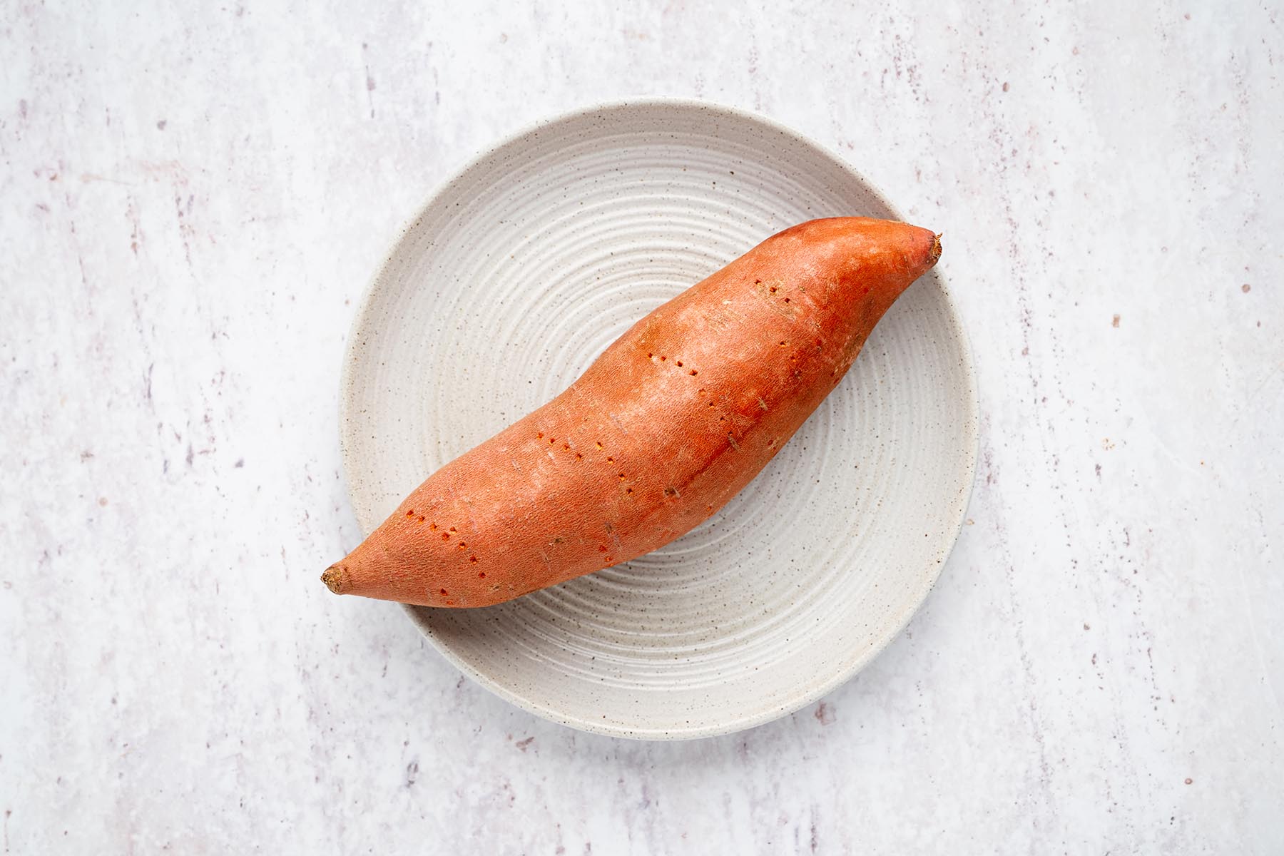 Sweet potato pierced several times with a fork and placed on a plate before cooking.