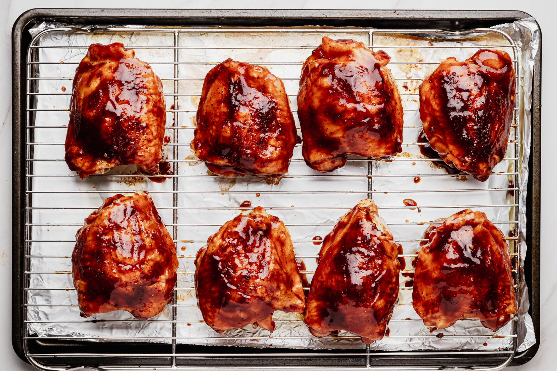 Partially baked chicken thighs brushed with barbecue sauce on a wire rack before returning to the oven to caramelize.