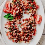 Overhead view of four bruschetta chicken cutlets topped with diced tomatoes, fresh basil, mozzarella pearls, and balsamic glaze on a white platter.
