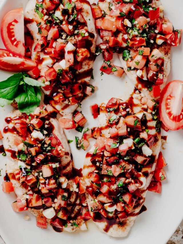 Overhead view of four bruschetta chicken cutlets topped with diced tomatoes, fresh basil, mozzarella pearls, and balsamic glaze on a white platter.