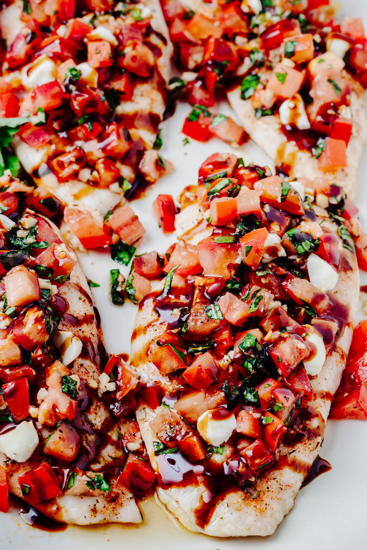 Close-up of bruschetta chicken topped with diced tomatoes, fresh basil, mozzarella pearls, and balsamic glaze.